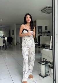 Lengvas, raštuotas pižamos komplektas kreminės spalvos su juodais žirafų raštais, viršuje su nėriniuotu apvadu ir jaukiais smėlio spalvos šlepetėmis. Lygi medžiaga, laisvas pjūvis.
