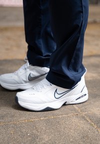 Sapatilhas brancas da Nike com detalhes em azul marinho, apresentando um design elegante, parte superior em malha, superfície texturizada e sola de borracha para aderência.