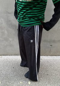 Czarne spodnie dresowe z białymi paskami po bokach, zestawione z zielono-czarną koszulką w paski. Gładka tkanina, luźny krój, widoczne logo.
