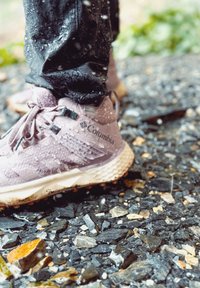 Lyse lilla vanntette sneakers med teksturert overflate, grå accenter og hevede mønstre, som hviler på en steinete, våt overflate.