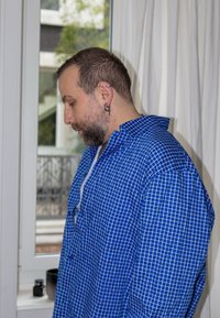 Chemise à carreaux bleue avec col et patte de boutonnage. Le tissu semble léger avec un motif en grille, porté par une personne vue de profil.
