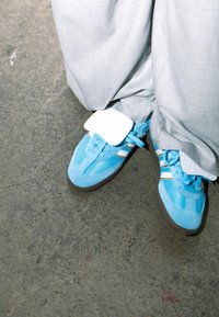 Μπλε αθλητικά παπούτσια από σουέτ και πλέγμα, με λευκές ρίγες και αποσπώμενη ζώνη, συνδυασμένα με γκρι χαλαρούς παντελόνες.