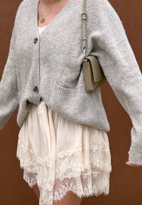 Szary, dziany kardigan z dekoltem w serek i dwoma guzikami, w zestawieniu z kremową spódnicą z koronkowym wykończeniem i delikatnym kwiatowym wzorem.
