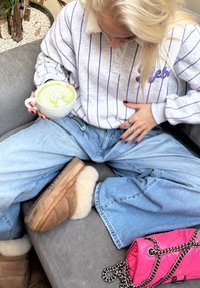 Sweat-shirt gris clair à rayures avec un col en peluche ; jean ample bleu clair ; bottes camel avec bordure en fourrure blanche ; tasse blanche avec art latte vert.