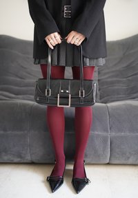 Sac à main en cuir noir de forme rectangulaire, avec quincaillerie argentée et design structuré. Porté avec une jupe plissée grise et des collants bordeaux.
