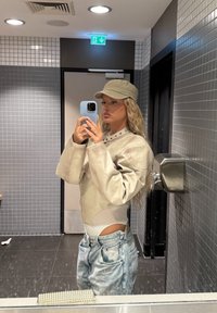 Beige læderjakke med overdimensionerede ærmer, høj krave detalje, parret med lyseblå slidte jeans og en lysegrøn kasket.