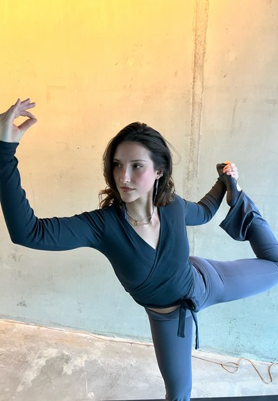 Top negro de manga larga con diseño cruzado y leggings gris de cintura alta; modelo en una pose dinámica que muestra la textura de la tela y el diseño ajustado.