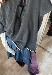 Svart oversized skjorta med ficka, lagerpålagd med en blå rutig kjol och lila vida byxor. Texturerade tyger och varierande längder är synliga.