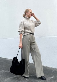 Svetlo bež pleteni pulover s turtleneck izrezom, ohlapnega kroja. Prilagojeni svetlo sivi hlače z naborki. Črna suknjična torba iz semiša, črne špicaste balerinke.