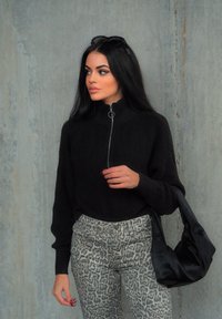 Μαύρο πλεκτό πουλόβερ με ψηλό γιακά και φερμουάρ, συνδυασμένο με γκρί τζιν με λεοπάρ μοτίβο. Κρατάει μια μαύρη σατέν �τσάντα ώμου.