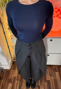 Camisa de manga larga color azul oscuro combinada con pantalones grises a rayas con un diseño de cruce único y dos botones negros en la cintura.