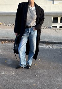 Μαύρο μακρύ παλτό πάνω από γκρι πουλόβερ, σε συνδυασμό με ανοιχτό μπλε τζιν. Η εμφάνιση ολοκληρώνεται με μαύρα παπούτσια και μαύ ρη τσάντα ώμου.