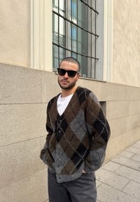 Ruda, pilka ir juoda argyle rašto kardiganas su užsegimu priekyje, minkšta tekstūra ir laisvas siluetas, derinamas su balta marškinėliais ir juodais akinių nuo saulės.