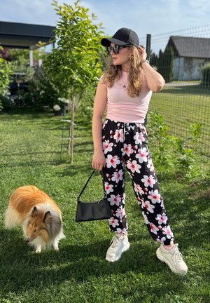 Pantalones de estampado floral negro con flores blancas y rojas, una camiseta ajustada rosa claro, gafas de sol, un bolso negro y zapatillas gruesas blancas.