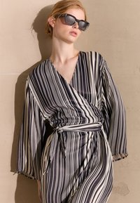 Abito avvolgente a righe bianche e nere in tessuto leggero con maniche lunghe, caratterizzato da un vita legata e una silhouette fluida.