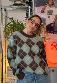 Übergroßer Pullover im hellgrünen und braunen Argyle-Muster, mit einem gerippten Rundhalsausschnitt und Bündchen, getragen über hochgeschnittenen Jeans.