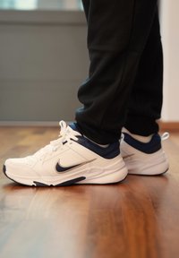White and navy athletic trainers with a textured finish, laces, and a smooth rubber sole. Features the Nike logo on the side and contrasting accents.
