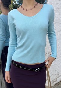 Lyseblå strikket sweater med V-udskæring og lange ærmer, parret med en tætsiddende lilla nederdel og et sort bælte med metalindsatser.