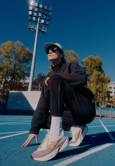 Zapatillas deportivas con un diseño ligero, mezcla de colores blanco hueso y lavanda, parte superior de tela texturizada y suela blanca prominente.