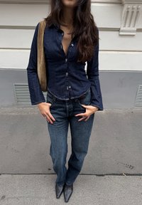 Sötét farmer ing, hosszú ujjal; magas derekú, bő szárú farmernadrággal párosítva, hegyes orrú fekete cipőkkel. Bézs válltáska.