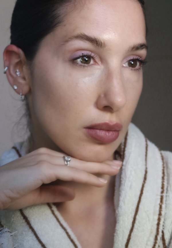 Donna con espressione neutra che poggia il mento sulla mano, indossando un indumento leggero a righe e molteplici piercing all'orecchio con anelli e borchie.