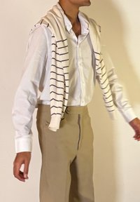 Άνδρας που φορά λευκό πουκάμισο με κουμπιά και μπεζ παντελόνι, με ένα κρεμ πουλόβερ με ναυτικές ρίγες περασμένο στους ώ μους.