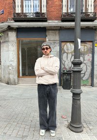 Person wearing a light plaid hooded jacket, black wide-leg jeans, and grey sneakers, standing beside a streetlight in an urban setting.