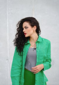 Zeleno platneno srajco s gumbi čez črno-bel karirast vzorec, v kombinaciji z zeleno pleteno krilo. Vidne so zlate obročaste uhane.