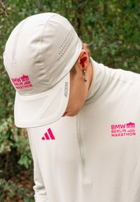 Light grey cap with mesh accents, featuring pink "BMW Berlin Marathon" and "ADIZERO" logos. Worn with a grey long-sleeve shirt.