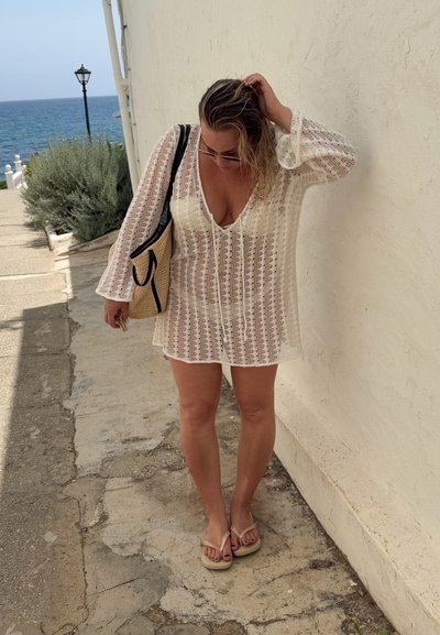 Vestido cubridor largo, ligero y blanco de manga larga con un escote en V profundo, que presenta patrones de ganchillo detallados y un corte holgado, combinado con chanclas.