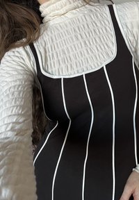 Vestito a righe bianche e nere sopra una maglia bianca a maniche lunghe con texture; il vestito presenta una scollatura quadrata con bordo bianco.