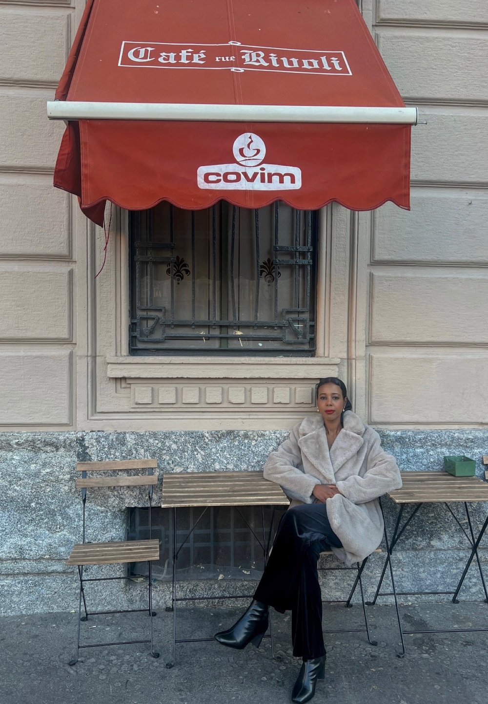 Punane varikatus, millel on "Café rue Rivoli" ja "covim" logod. Pehme beež sulejope, mustad püksid ja kõrged kontsakingad puidust pingil.