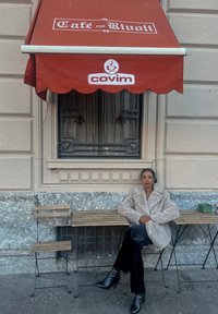Punane varikatus, millel on "Café rue Rivoli" ja "covim" logod. Pehme beež sulejope, mustad püksid ja kõrged kontsakingad puidust pingil.