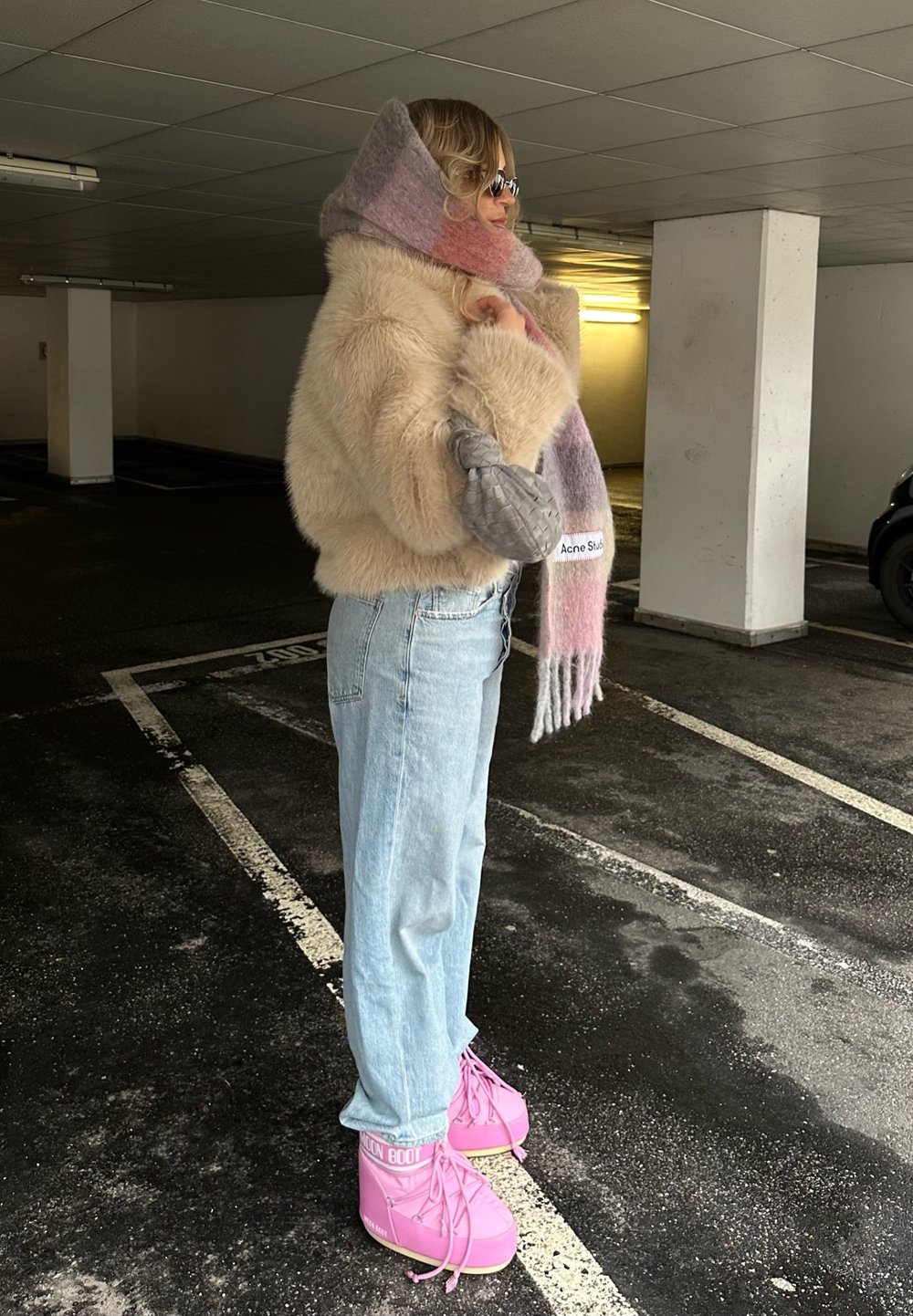 Faux fur beige jas, gelaagde pastel sjaal, lichtblauwe straight-leg jeans en roze veterschoenen met logo-accenten.