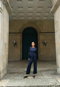 Marinblå koordinerad outfit som består av en långärmad topp och vida byxor, tillsammans med svarta öppna skor. Texturerad stensbakgrund.