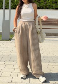 Bézs, csíkos, bőszárú nadrág redőkkel; egy fehér bordázott ujjatlan felsővel párosítva. Krémszínű horgolt kézitáskát tart, és világos tornacipőt visel.