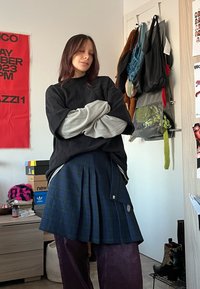 Svart oversized sweatshirt över en grå långärmad tröja, matchad med en blårutig plisserad kjol och mörklila byxor.