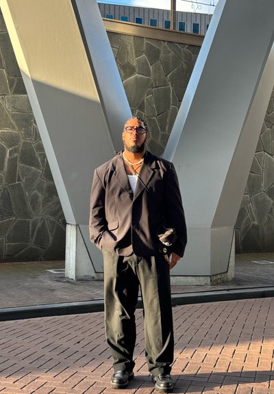 Blazer negro de corte amplio sobre una camiseta blanca, combinado con pantalones negro holgados y zapatos negros gruesos; una pequeña bolsa cuelga del hombro.