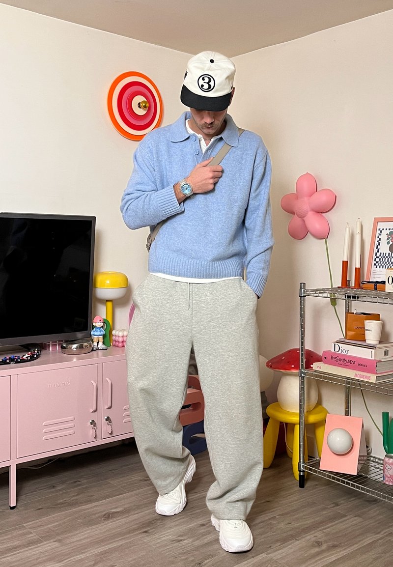 Maglione azzurro chiaro in maglia con colletto, pantaloni della tuta grigi e scarpe da ginnastica bianche. Un cappello classico e un orologio completano l'abbigliamento casual.