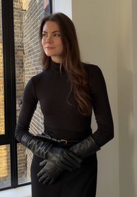 Gants en cuir noir avec une texture lisse et un design minimaliste, portés avec un col roulé noir ajusté et une ceinture noire.