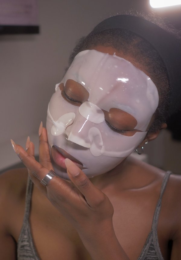 Hydrogeelinaamio kasvoilla, läpinäkyvä valkoisin yksityiskohdin. Pitkät kynnet ja hopeinen sormus näkyvissä. Harmaa toppi osittain esillä.