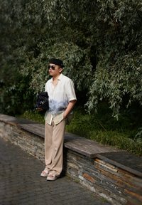 Τζιν με κοντό μανίκι με σχέδιο τοπίο σε μπλε-άσπρο χρώμα, μπεζ παντελόνι σε φαρδιά γραμμή, υπερμεγέθη μαύρη τσάντα και ανοιχτόχρωμες σάνταλες.