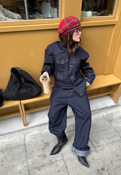 Chaqueta vaquera y pantalones de pierna ancha en lavado oscuro con costuras rojas contrastantes. Botas negras puntiagudas, boina de cuadros roja y bolso negro.