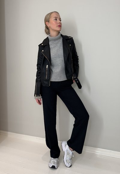 Chaqueta de biker de cuero negro, suéter de cuello alto gris, pantalones azul marino a rayas y zapatillas plateadas con suela gruesa. Look limpio y casual.