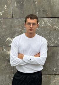 Camisa de algodão branca de mangas longas com decote redondo, combinada com calças de atletismo pretas e texturizadas; detalhe de logótipo circular na manga.