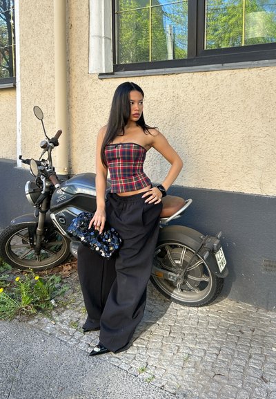 Pantalones anchos negros, top sin tirantes de cuadros rojos y azules, cartera texturizada negra con lentejuelas y zapatos negros brillantes de punta; motocicleta de fondo.