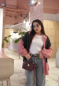 Túlságosan nagy szürke kardigán piros csíkozású ujjakkal, fehér felső, magas derekú farmernadrág, arany övcsat és egy kis bordó kézitáska.