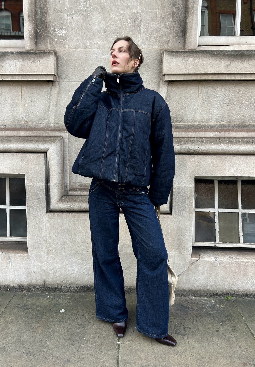 Zils džinsa pūkains jaka ar augstu apkakli un tumšas plataji piegriezuma džinsi. Apģērbam ir kontrastējošas šuves un brūnas zābaki ar papēdi.