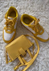 Gula sneakers med vita accenter, texturerad gummisula, och en matchande gul väska med en slät yta och justerbar rem.