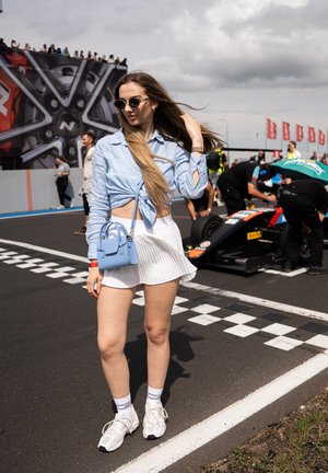 Camisa celeste de botones atada a la cintura, falda blanca con pliegues y un pequeño bolso azul. Zapatillas grises y calcetines blancos hasta el tobillo completan el conjunto.